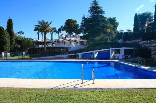 a large blue swimming pool with palm trees and a building at Casa Dancha in Mijas Costa