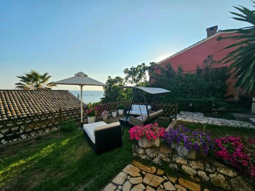 um pátio com um guarda-sol, cadeiras e flores em Corfu Glyfada Beach Apartment 59 em Glyfada