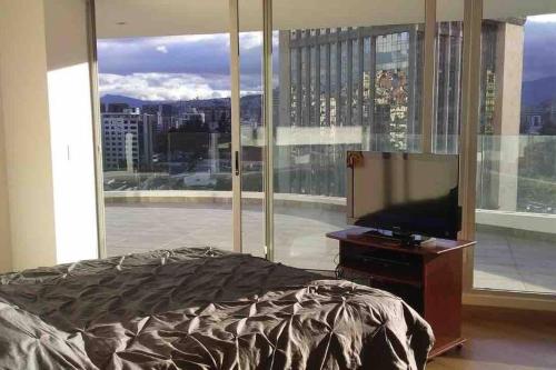 1 dormitorio con 1 cama y TV frente a una ventana en El mejor balcón y vista de Quito en el Parque la Carolina Coliving Ecuador, en Quito