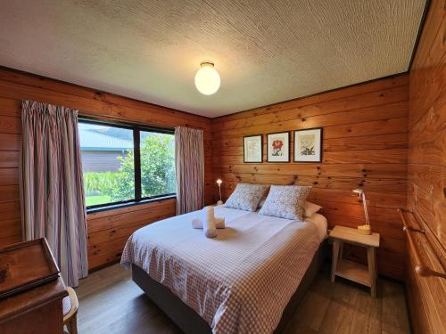 a bedroom with a bed with wooden walls and a window at Kotare Cottage Hahei in Hahei