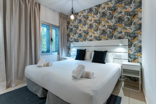- une chambre avec un grand lit blanc et un mur fleuri dans l'établissement Tajinaste Beach Gay Men Only, à Playa del Ingles