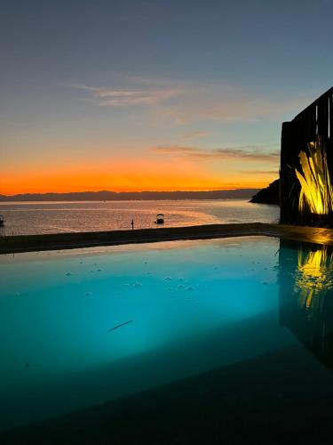 a swimming pool with a view of the ocean at sunset at Casa da Ilha in Praia de Araçatiba