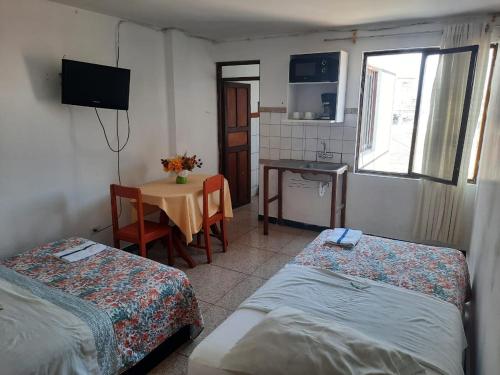 a room with two beds and a table and a kitchen at Hostal San Antonio in Chimbote