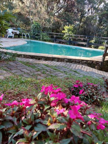 a swimming pool with pink flowers in front of it at Pousada Anecuém in Monte Verde