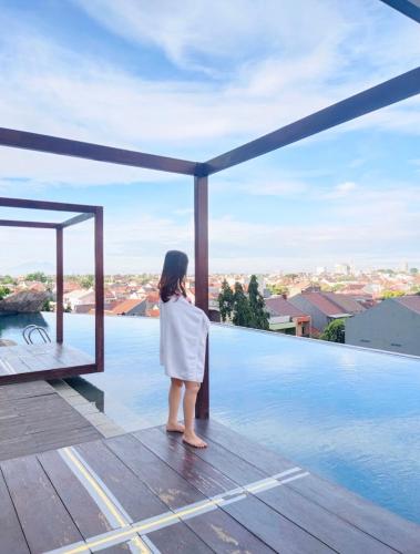 une femme debout sur une terrasse donnant sur une piscine dans l'établissement Grand Kamala Lagoon Bekasi Apartement - Type Studio, à Pulosirih