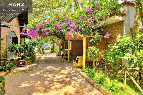einen Backsteinweg, der zu einem Haus mit lila Blumen führt in der Unterkunft HANZ AND Sunset Beach Resort in Phu Quoc