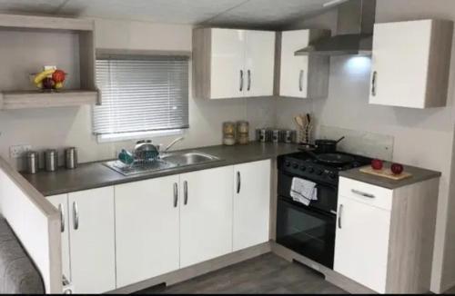 a kitchen with white cabinets and a sink and a stove at Greenhouse 24 in Little Clacton