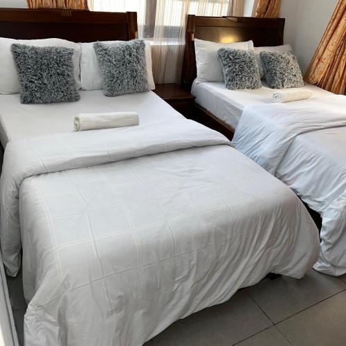 2 camas en una habitación con sábanas y almohadas blancas en En-Suite Rooms W/Pool & Gym in Mikocheni Near Beach, en Dar es Salaam