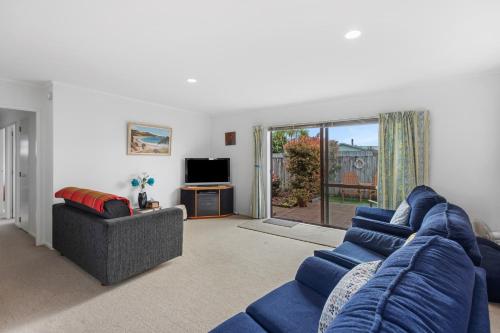 a living room with a blue couch and a tv at Riviera Casa - Mount Maunganui Holiday Home in Mount Maunganui
