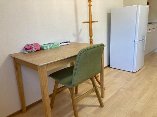 a wooden table with a green chair and a refrigerator at Midori Guesthouse&Hostel in Tsushima