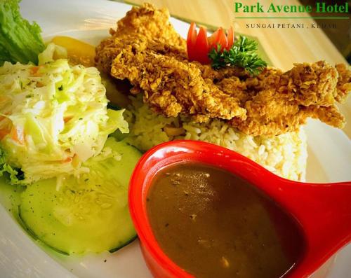 a plate of food with meat and rice and a sauce at Park Avenue Hotel Sungai Petani in Sungai Petani