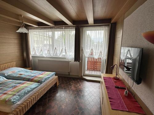 a bedroom with a bed and a tv and windows at RELAX Seefeld Apartman in Seefeld in Tirol