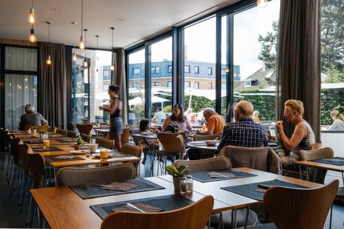 people sitting at tables in a restaurant with large windows at Cosy Cottage Apostroff in Koksijde