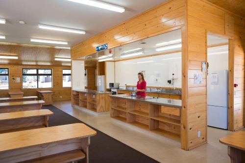 a woman in a kitchen with wooden walls and tables at Fox Glacier TOP 10 Holiday Park & Motels in Fox Glacier