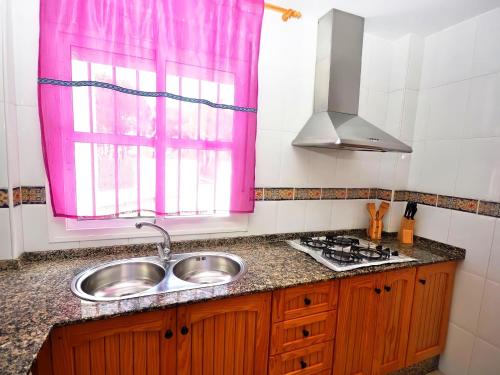 une cuisine avec un évier et une fenêtre rose dans l'établissement Apartamento junto al mar Piscina solo familias, à Conil de la Frontera