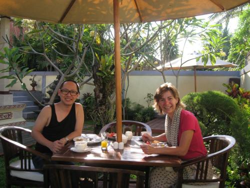 two women sitting at a table under an umbrella at Frangipani Homestay in Nusa Dua