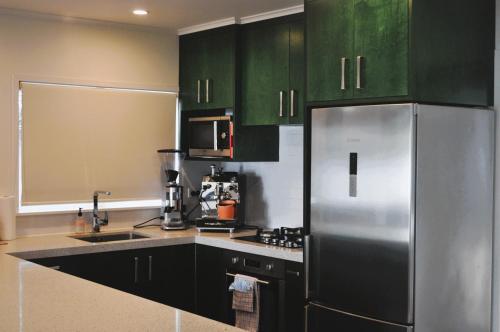 a kitchen with green cabinets and a stainless steel refrigerator at Lakeside Cottage with Jetty at Lake Tarawera in Rotorua