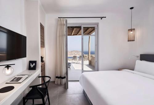 a white bedroom with a bed and a desk with a computer at Radisson Blu Euphoria Resort, Mykonos in Kalo Livadi