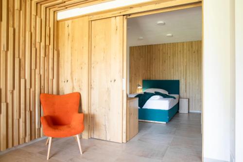 a bedroom with a bed and a orange chair at Amenity Hotel & Resort Lipno in Lipno nad Vltavou