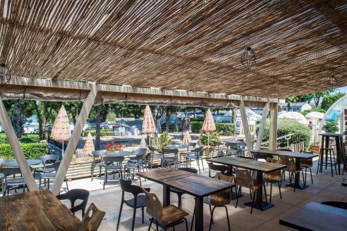a restaurant with tables and chairs under a straw roof at Parc du Charouzech in Salles-Curan