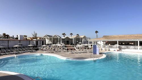ein großer Pool mit Stühlen und Tischen in einem Hotel in der Unterkunft Caleta Dorada in Caleta de Fuste