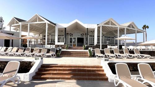 a building with white chairs and tables and umbrellas at Caleta Dorada in Caleta De Fuste