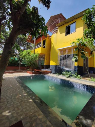 a swimming pool in front of a yellow house at Redstone House by Oxystays Hospitality in Ganpatipule