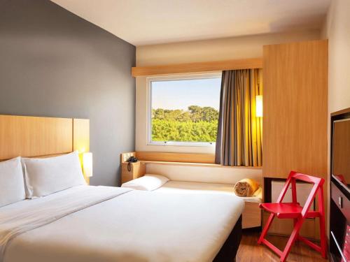 une chambre d'hôtel avec un lit et un fauteuil rouge dans l'établissement ibis Piracicaba, à Piracicaba