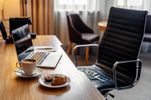 a laptop on a table with a cup of coffee and a pastry at Hotel Haffner Resort & Spa - Destigo Hotels in Sopot