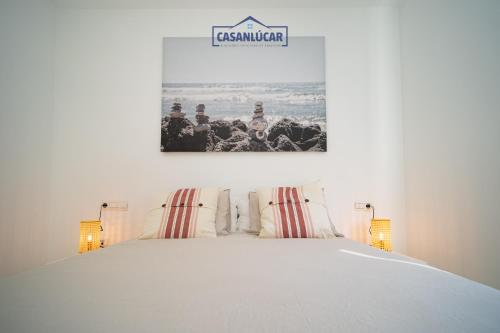 een slaapkamer met een wit bed met een bord aan de muur bij Vivienda Magallanes in Sanlúcar de Barrameda