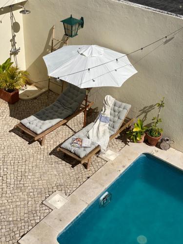 an umbrella and two chairs next to a swimming pool at Beach house upscale villa with pool in Costa da Caparica