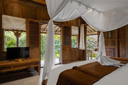 Moringa Ubud Villa في أوبود: غرفة نوم مع سرير مع مظلة وتلفزيون