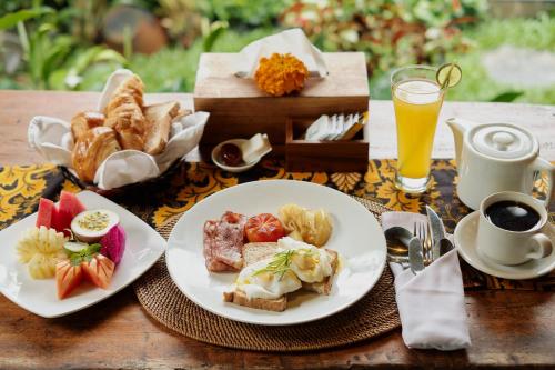 uma mesa com dois pratos de alimentos para o pequeno-almoço e um copo de sumo de laranja em Moringa Ubud Villa em Ubud