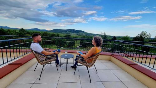 a man and woman sitting at a table on a balcony at Hotel Kőporos Hercegkút in Hercegkút