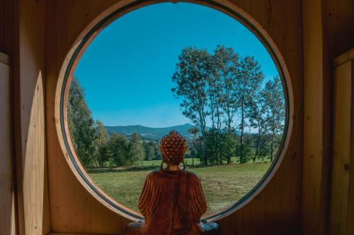 a person sitting in a room looking out a round window at Meadowland Samota Stříbrník in Žibřidice