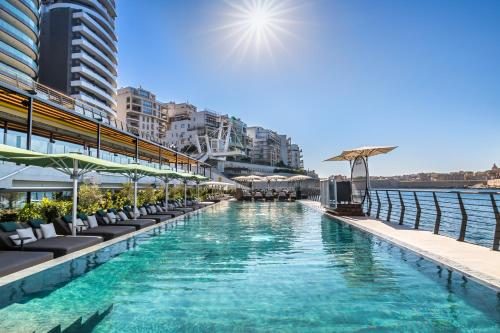 a swimming pool with chairs and umbrellas next to the water at Barceló Fortina Malta in Sliema