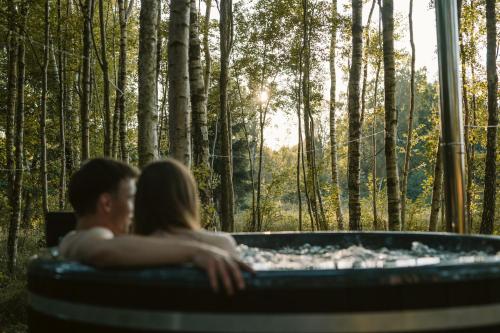 un hombre y una mujer sentados en un jacuzzi en un bosque en Czas na Las, en Żarnowska