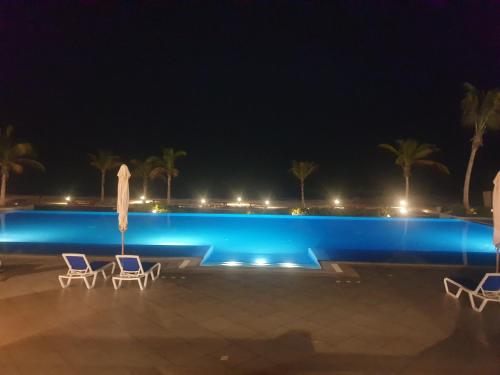 a pool at night with two chairs and a umbrella at Sunrise Sifah in As Sīfah
