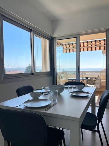 une salle à manger avec une table, des chaises et des fenêtres dans l'établissement Tout proche gare et port, vue mer, clim et parking, à Bandol