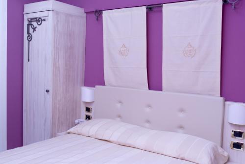 a white bed with purple walls and white curtains at Palazzo Reginella in Bovalino Marina