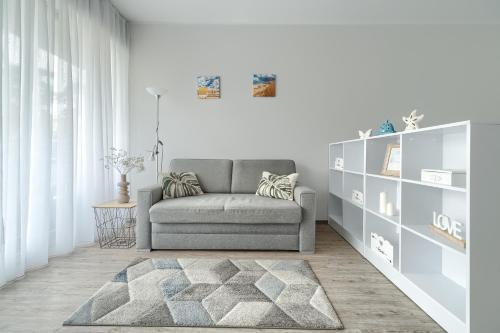 a living room with a gray couch and a book shelf at Apartament Doris 3- Studio z wanną in Pobierowo