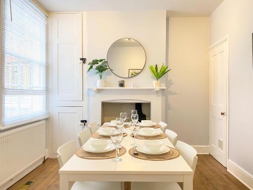 a white dining room with a table and a mirror at Stylish 3-bedroom home in Canterbury City-Centre - Superb Location! in Canterbury