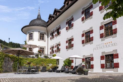 a large white building with tables and umbrellas at Aparthotel Ansitz Felsenheim in Lermoos