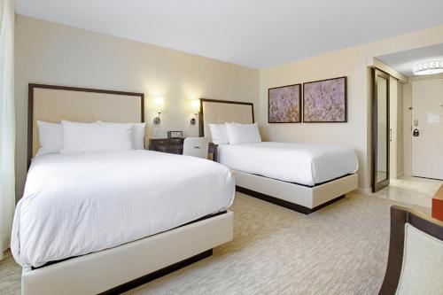 two beds in a hotel room with white sheets at The H Hotel in Midland