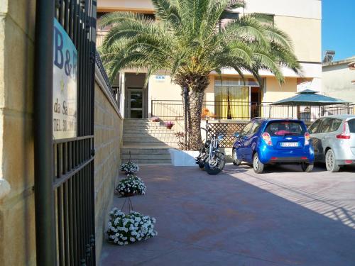 una macchina blu parcheggiata di fronte a un edificio con una palma di B&B Salvatore Lido di Noto a Noto Marina