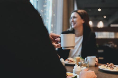 Una donna seduta a un tavolo che beve da una tazza di caffè di Quality Hotel River Station a Drammen