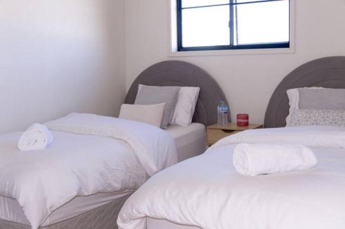 a room with two beds with white sheets and a window at Sunny & Spacious Family Retreat in Prestons