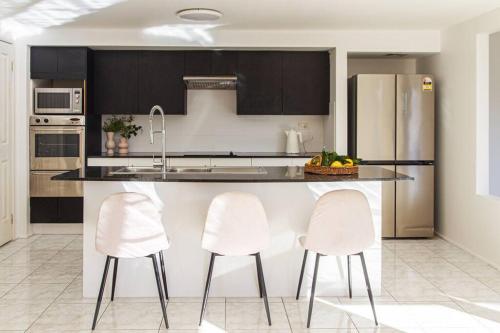 una cocina con 2 sillas blancas y una barra en Sunny & Spacious Family Retreat, en Prestons