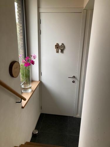 a hallway with a door with a vase of flowers on a shelf at Gastenverblijf Chambre dAmis in Heers