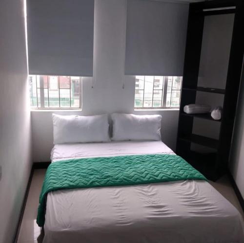 a bedroom with a bed with green sheets and two windows at Hotel Bogotá Suites in Bogotá